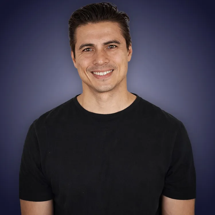Man with crossed arms wearing a black Tether shirt standing confidently in front of a wall with Tether logos.