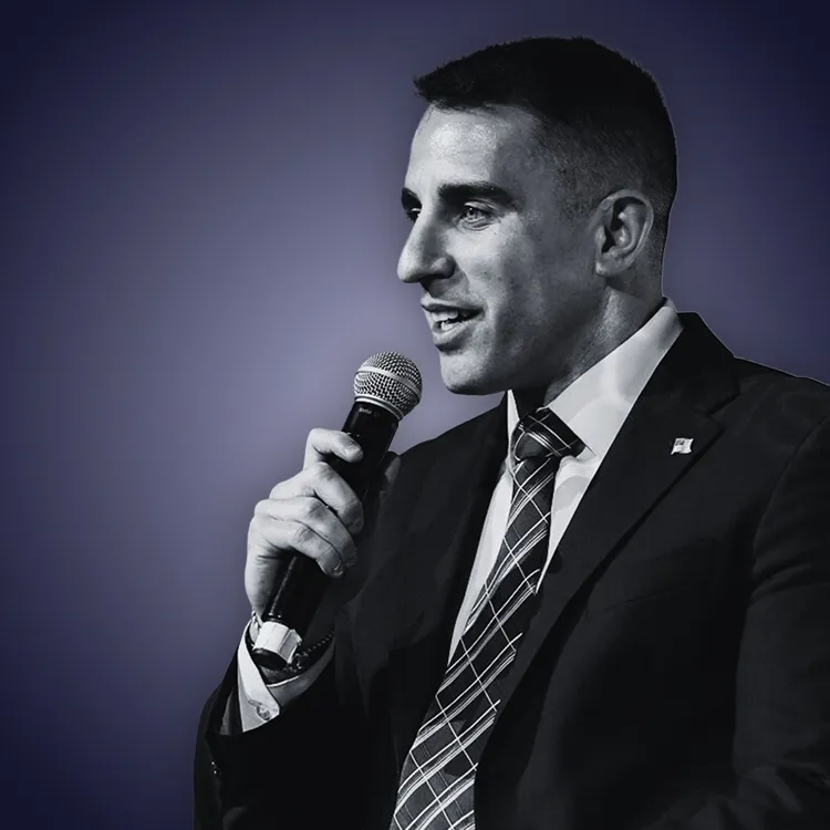 Man with crossed arms wearing a black Tether shirt standing confidently in front of a wall with Tether logos.