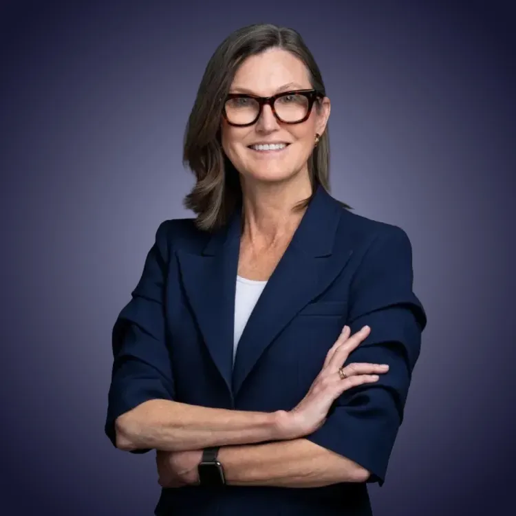 Man with crossed arms wearing a black Tether shirt standing confidently in front of a wall with Tether logos.