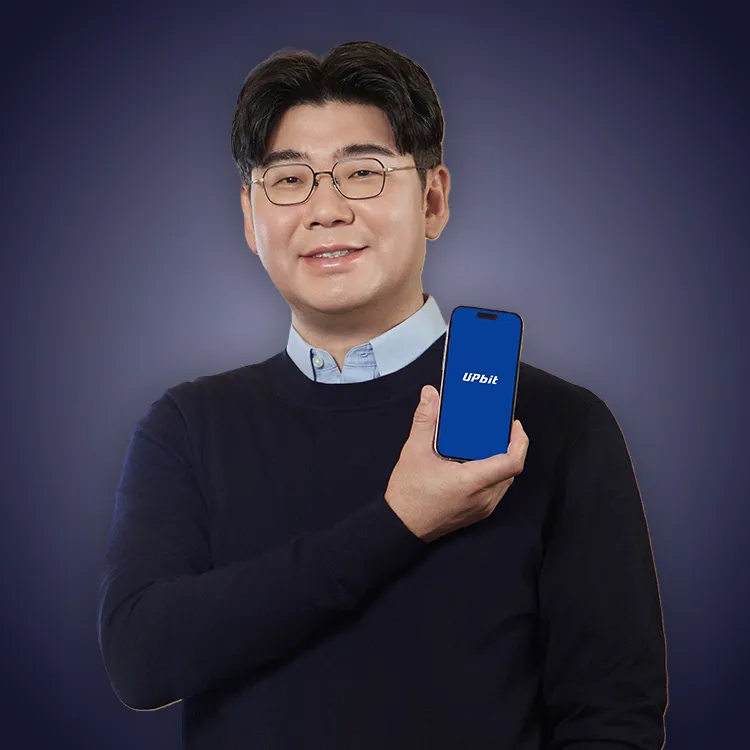 Man with crossed arms wearing a black Tether shirt standing confidently in front of a wall with Tether logos.