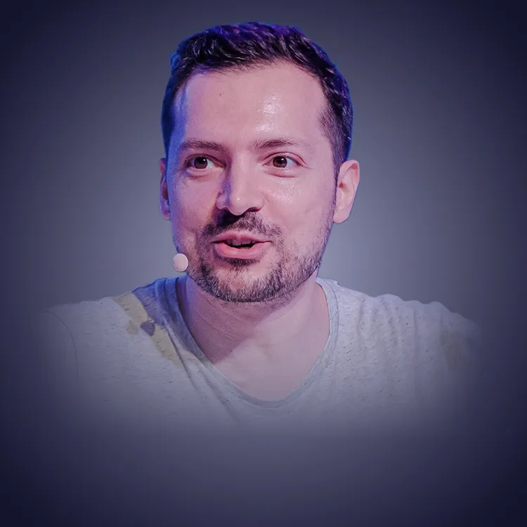 Man with crossed arms wearing a black Tether shirt standing confidently in front of a wall with Tether logos.