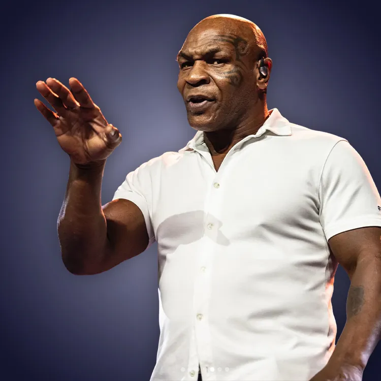 Man with crossed arms wearing a black Tether shirt standing confidently in front of a wall with Tether logos.