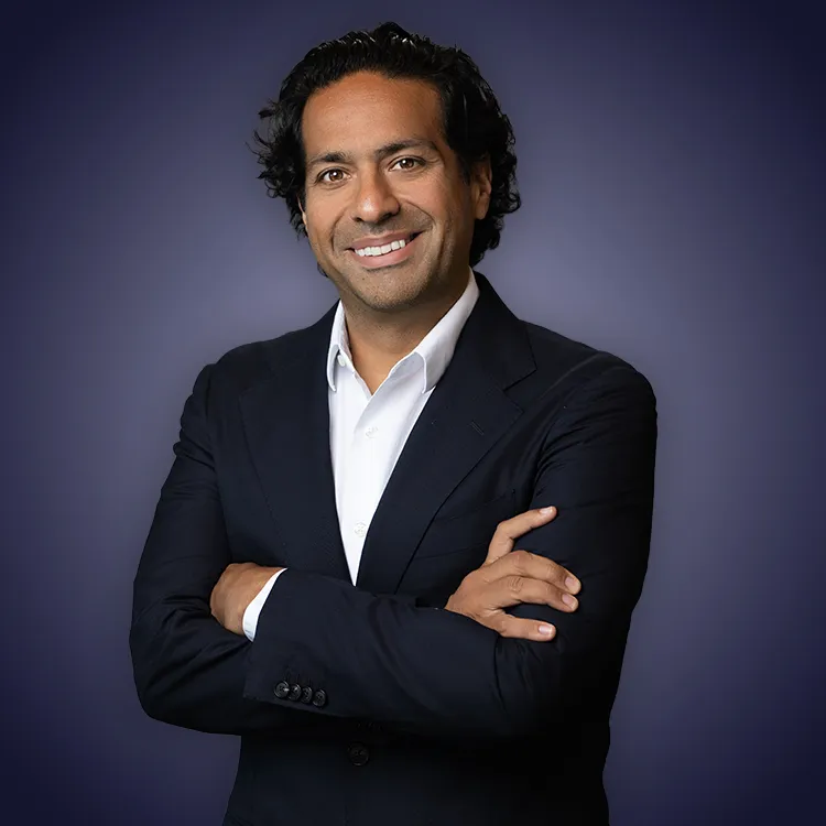 Man with crossed arms wearing a black Tether shirt standing confidently in front of a wall with Tether logos.