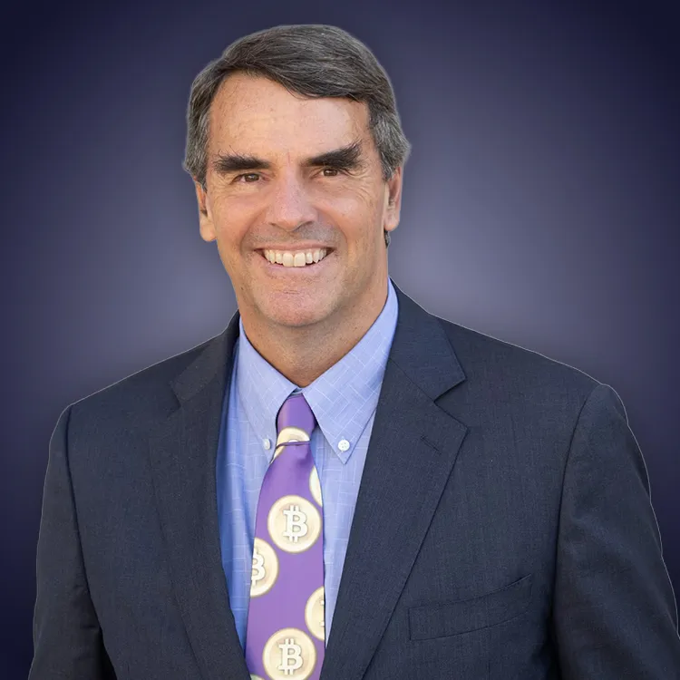 Man with crossed arms wearing a black Tether shirt standing confidently in front of a wall with Tether logos.